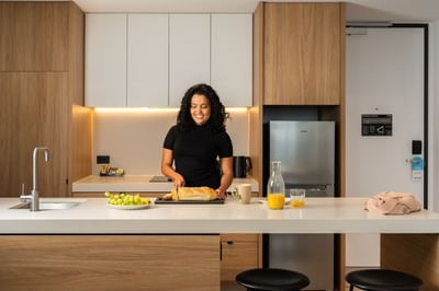 A lady cooking a meal in the Room kitchen at Nesuto Docklands