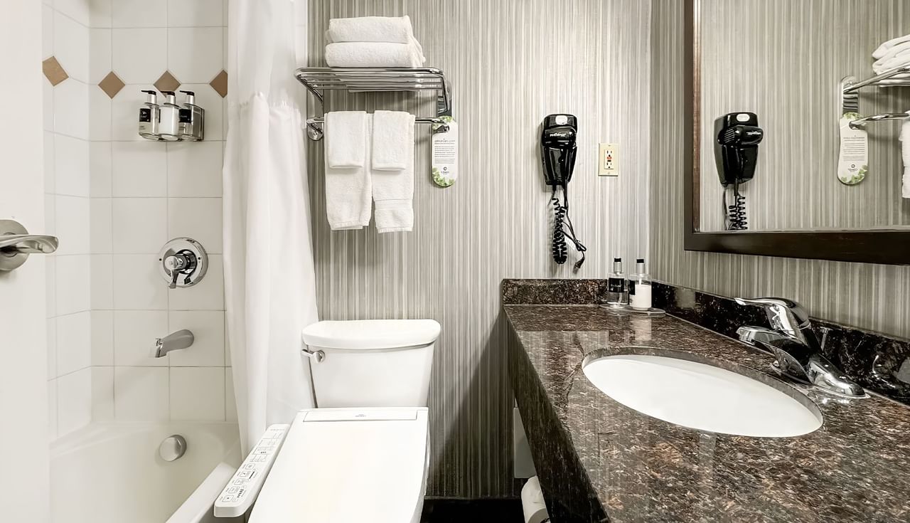 Hotel washroom with toilet, bathtub, sink, towels, and soap