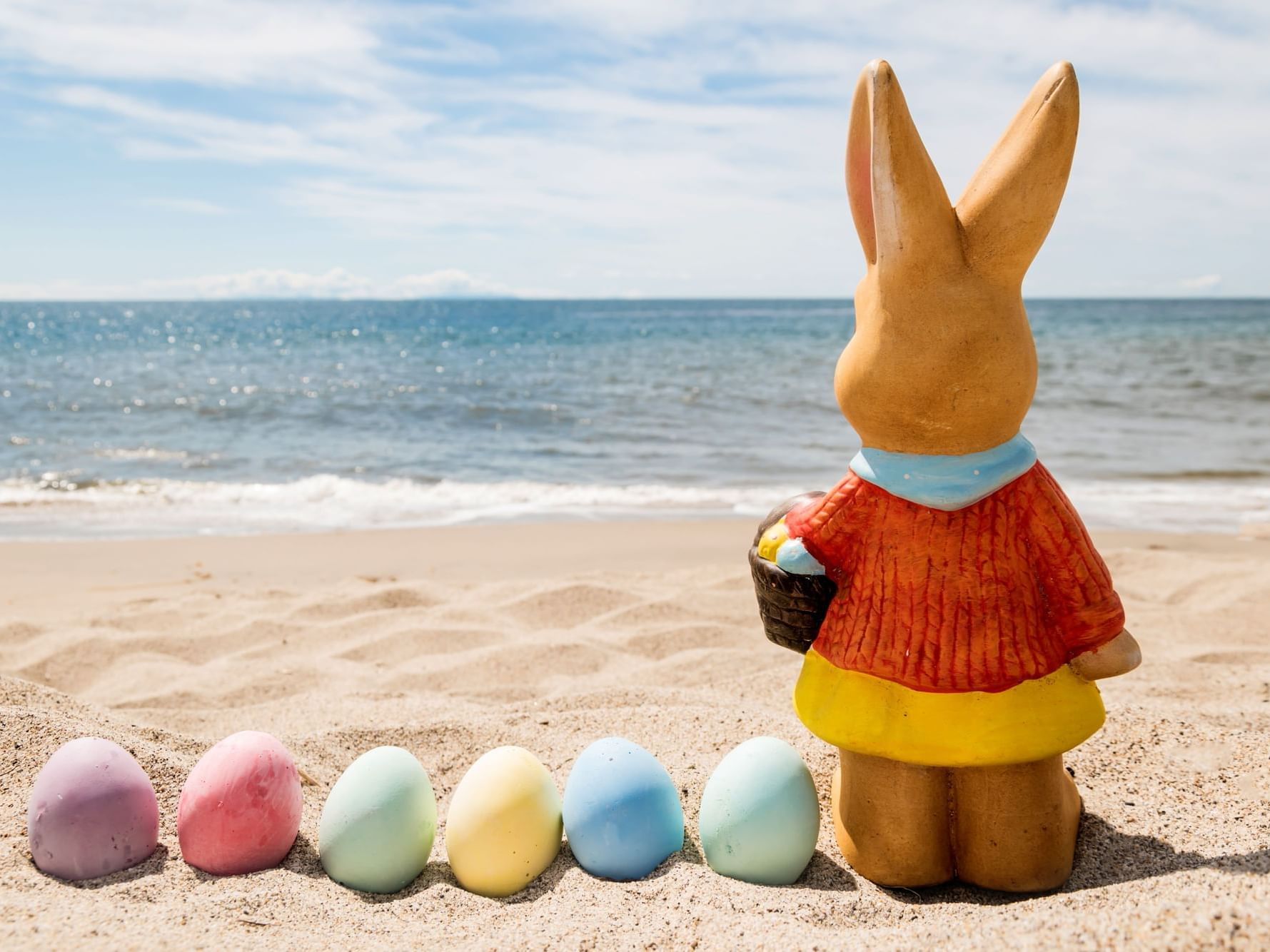 Rabbit statue stands on a beach near Ana Hotels Europa Eforie Nord, overlooking the ocean, with colored eggs in the sand