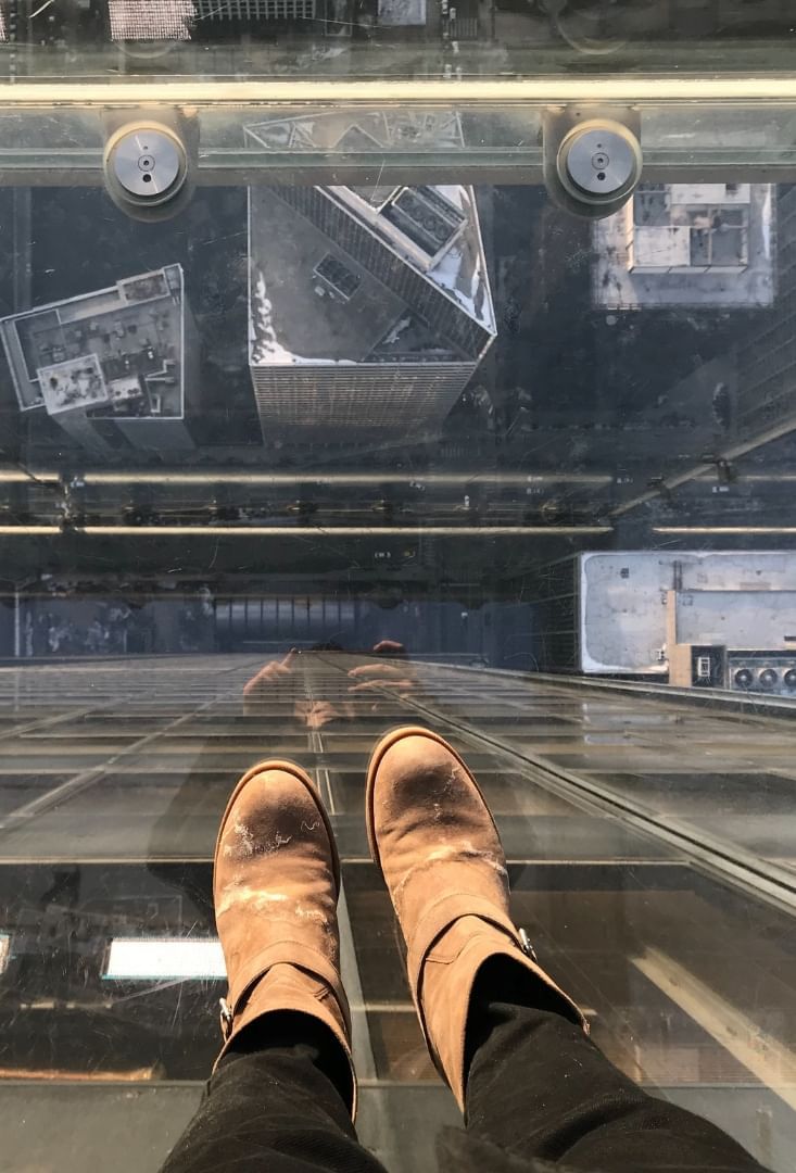 View from Skydeck Chicago glass ledge with boots above city buildings and busy streets below, near Hotel Saint Clair