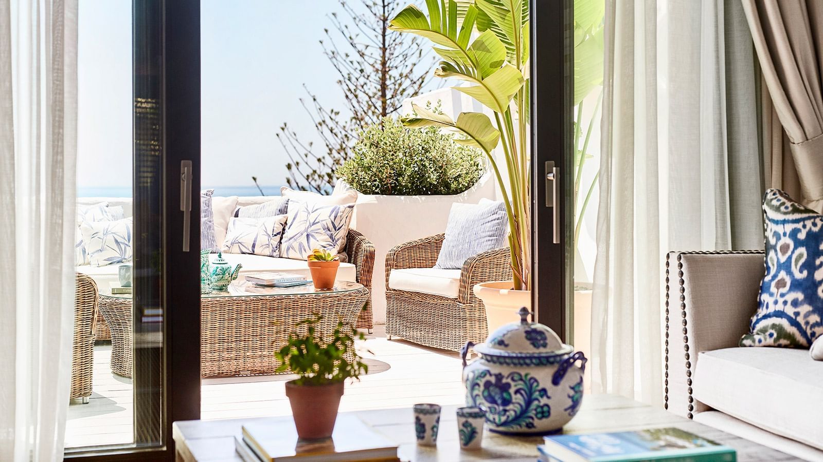 Imperial Beach Suite terrace with wicker lounge furniture, tropical plants, & blue patterned ceramics at Marbella Club