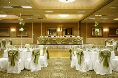 Banquet room setup with round dining tables and green ribbon chair covers facing head table at Clayton Plaza Hotel