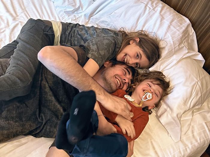 Famiglia felice, papà con figlie, che si rilassa sul letto a DUPARC Contemporary Suites