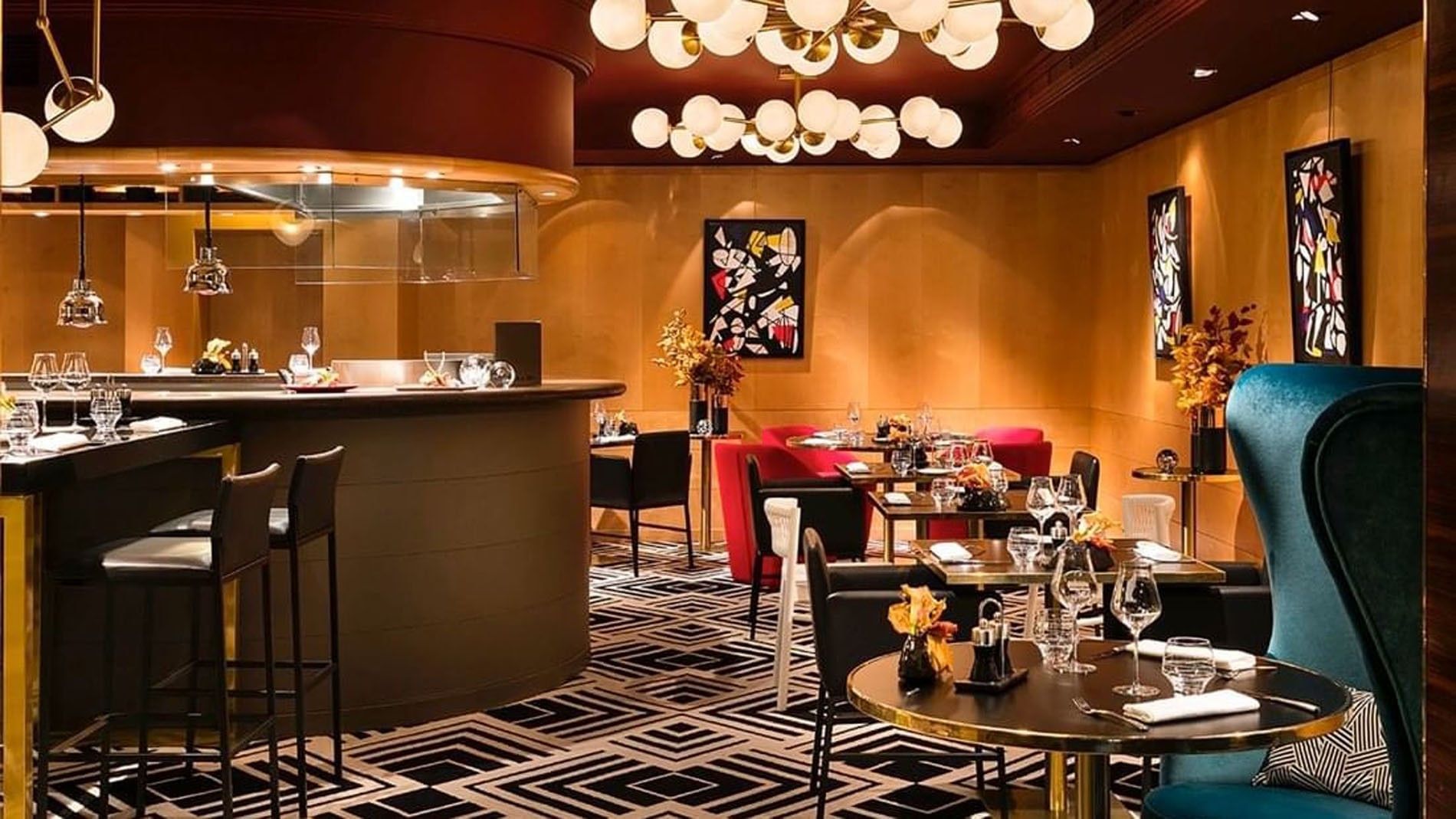 A restaurant dining area with a bar, tables, and chairs, featuring modern lighting and artwork.