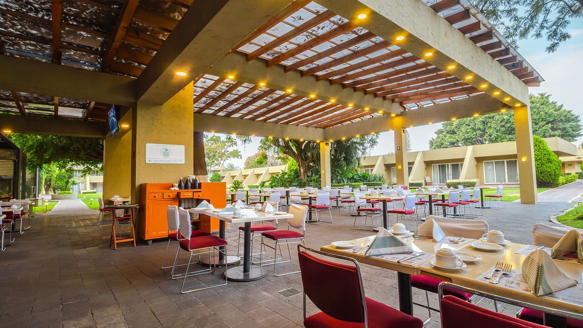 Outdoor patio dining in La Huerta featuring a wooden pergola and tables overlooking the garden at Camino Real Guadalajara