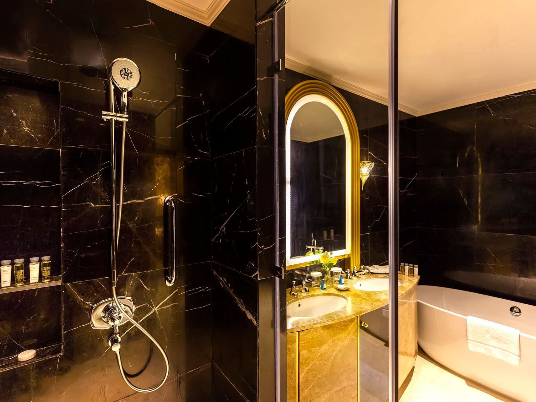 Elegant bathroom with black marble walls, a large bathtub, double sink, and a shower with a handrail.