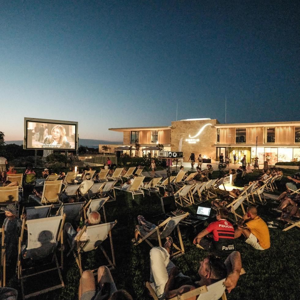 People watching a movie on a large screen outdoors at Cinema Under the Stars event.