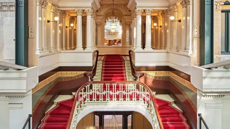A grand staircase with red carpet at Fullerton Hotel Sydney