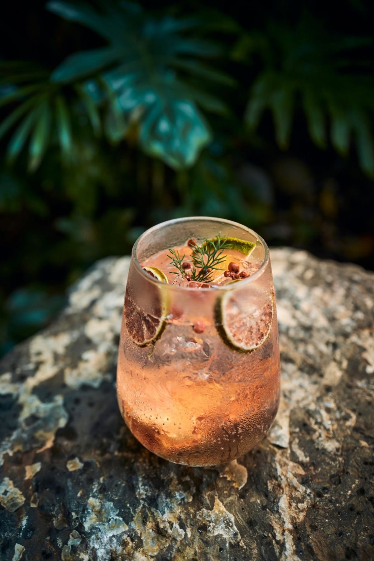 Refreshing pink gin cocktail garnished with dried citrus and herbs on a stone bar served at Cala Luna Boutique Hotel