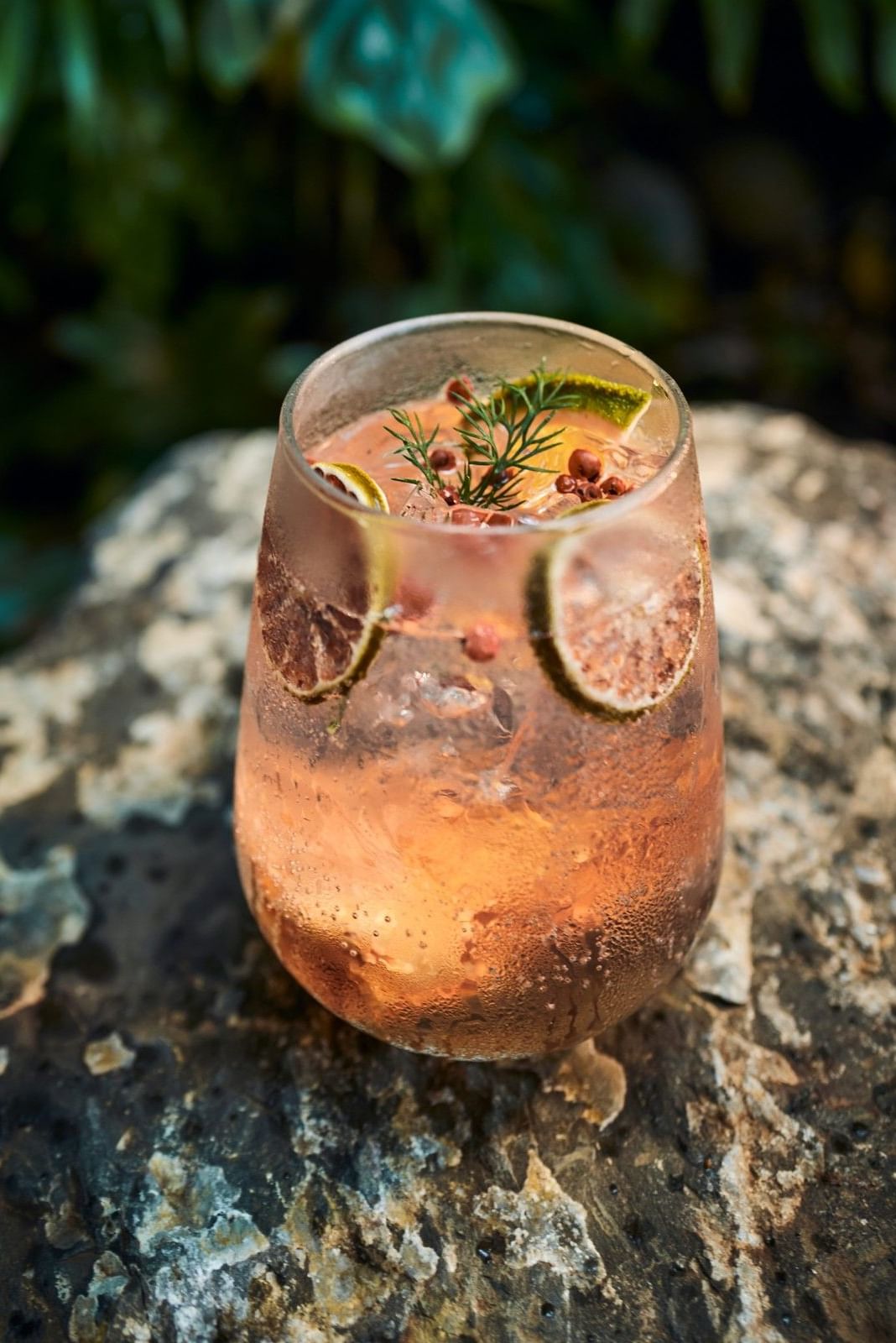 Refreshing pink gin cocktail garnished with dried citrus and herbs on a stone bar served at Cala Luna Boutique Hotel