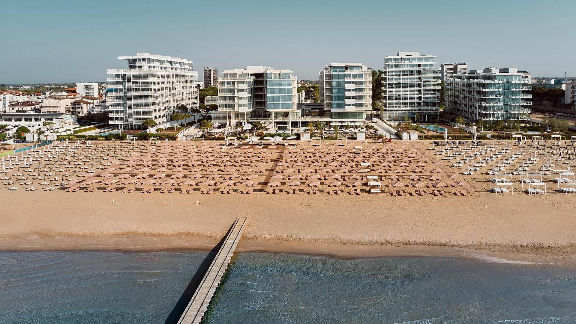 Spiaggia piena di ombrelloni e lettini vicino a un complesso di edifici moderni.