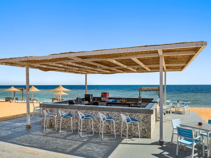 Beach bar with blue chairs under a thatched roof overlooking the ocean.