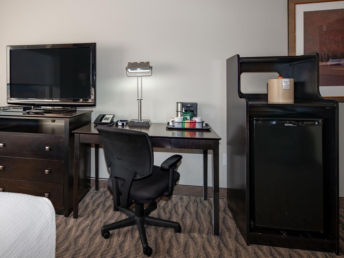 Hotel room with bed, desk, TV, and mini-fridge.
