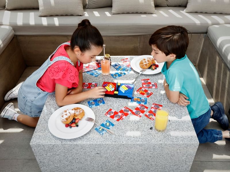 Two children playing a board game at a table with snacks and drinks at Grand Fiesta Americana