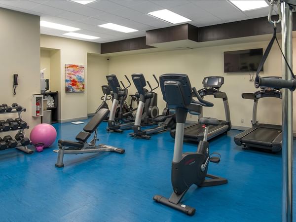 Fitness Centre with cardio equipment, free weights, and blue flooring at Coast Calgary University Area Hotel by APA.