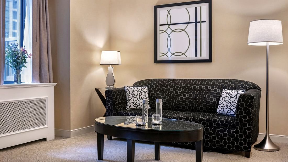 Black pattern sofa near floor lamp and hanging wall art in Premium Suite Two Queen Beds at Warwick Allerton Chicago