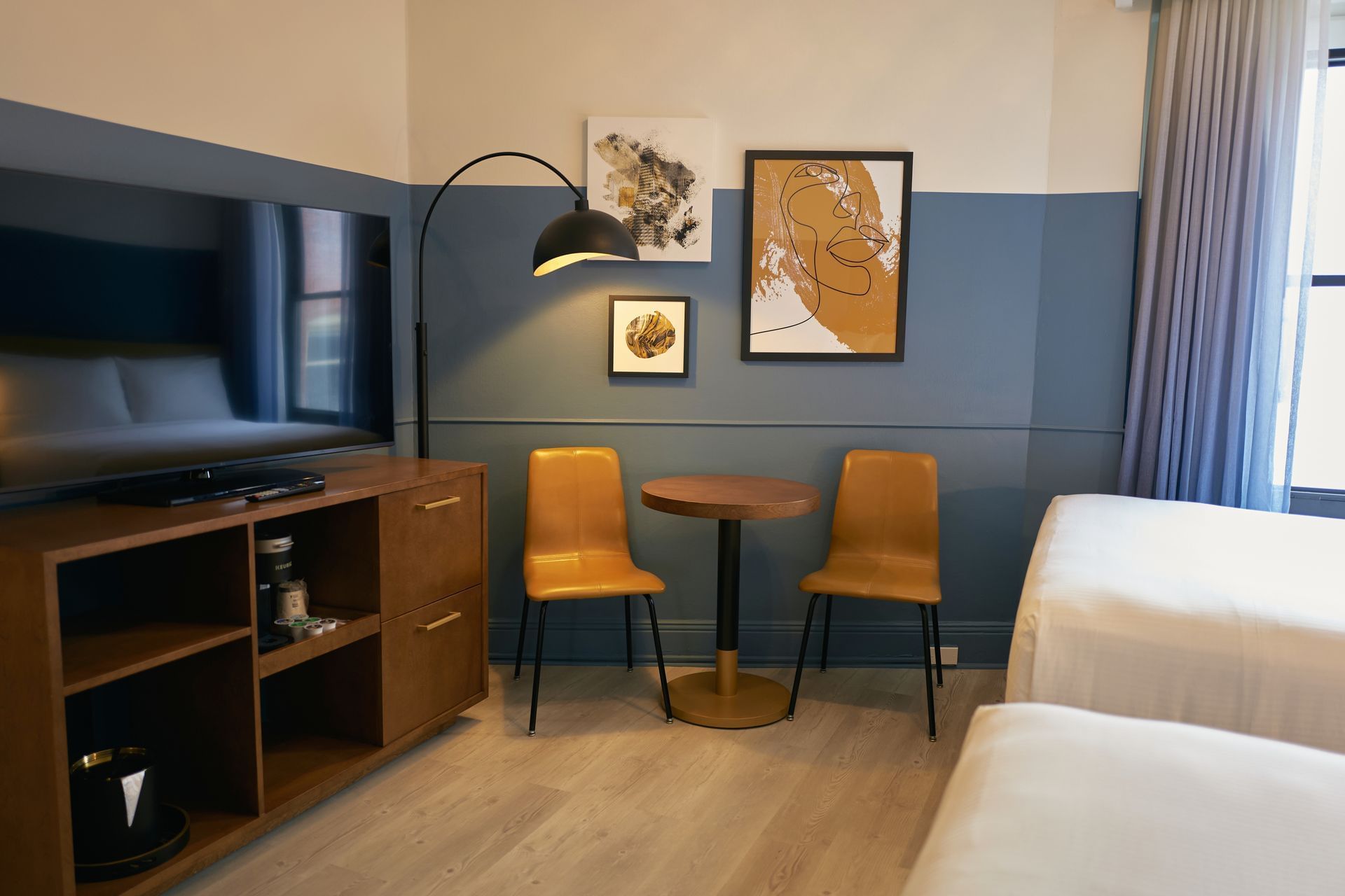 A hotel room with a TV, table, chairs, and artwork on the wall.