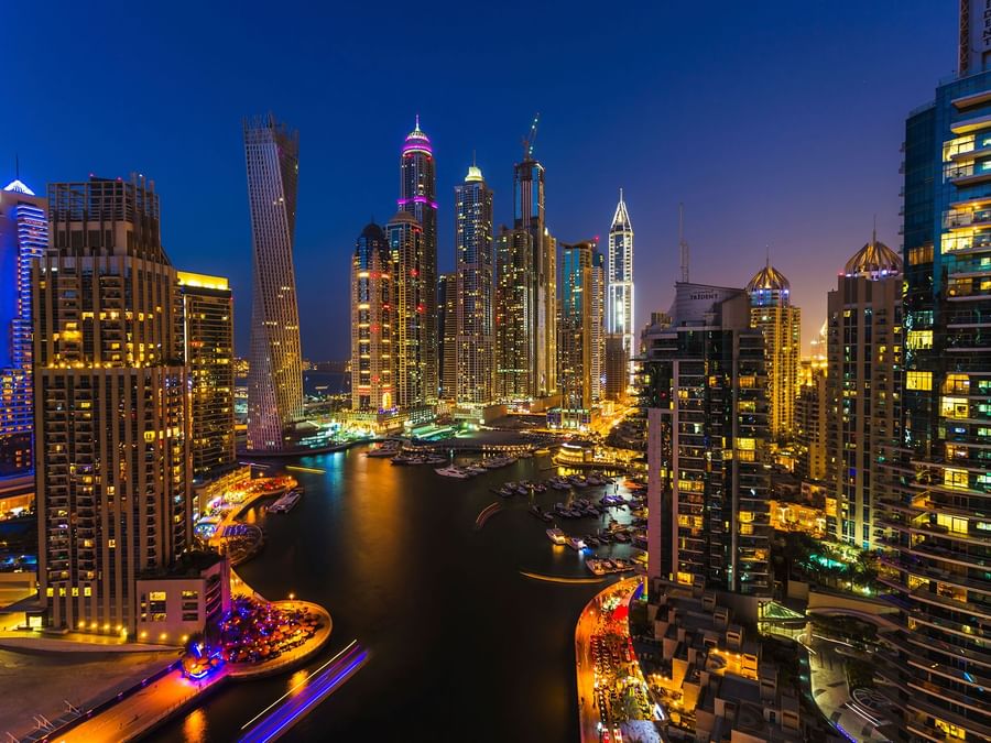 Twilight cityscape with illuminated skyscrapers along a waterfront near DAMAC Maison Aykon City, a luxury hotel in Dubai