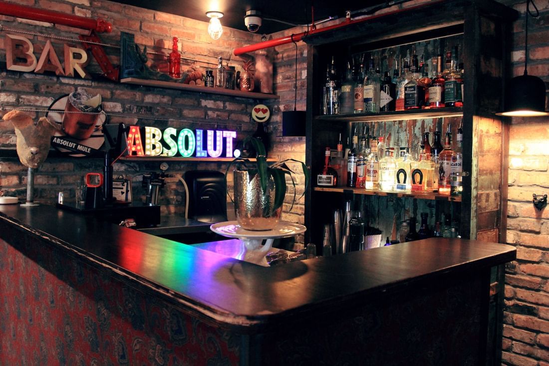 A dimly lit bar with a black counter, brick walls, and colorful neon lights.
