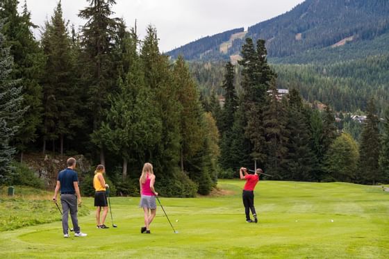 Family playing golf on a lush green course with mountains in the backdrop near Blackcomb Springs Suites