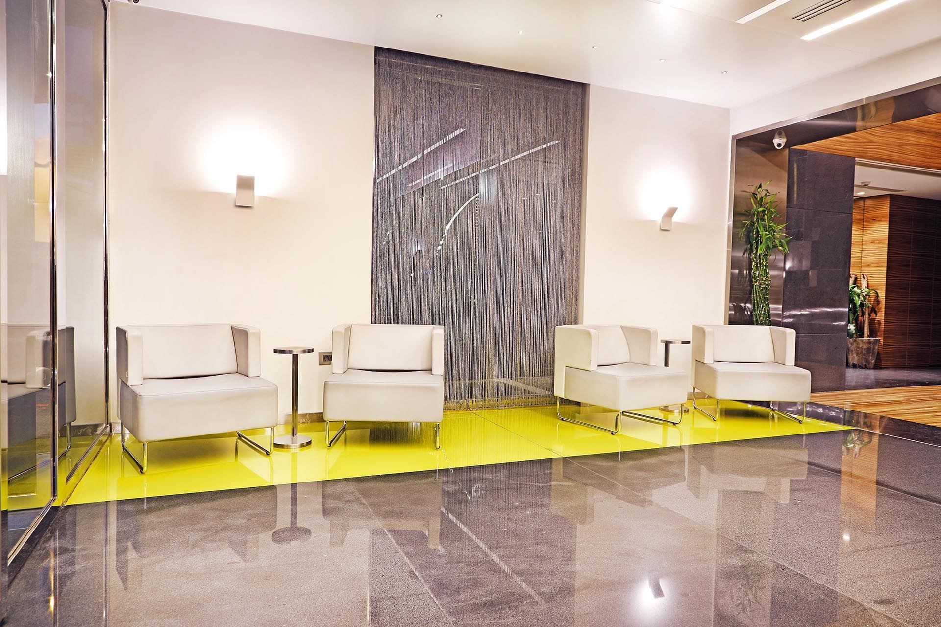 White armchairs by metal side tables on a yellow floor near a silver curtain at Warwick Stone 55 - Beirut