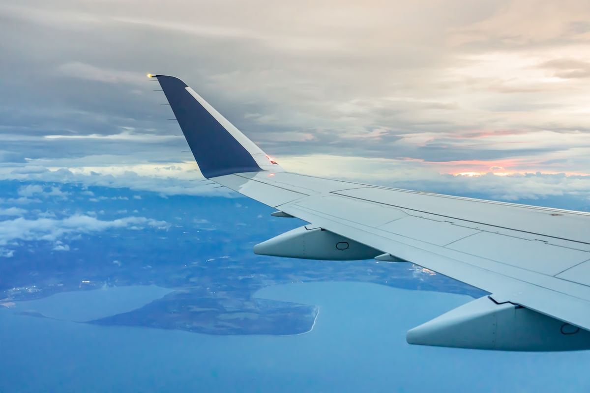 View of an airplane wing over a blue lake by coastal land under a cloudy sky near Warwick Seattle