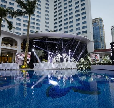 White tables and chairs arranged by a reflective pool, facing a decorated stage at Hanoi Daewoo Hotel