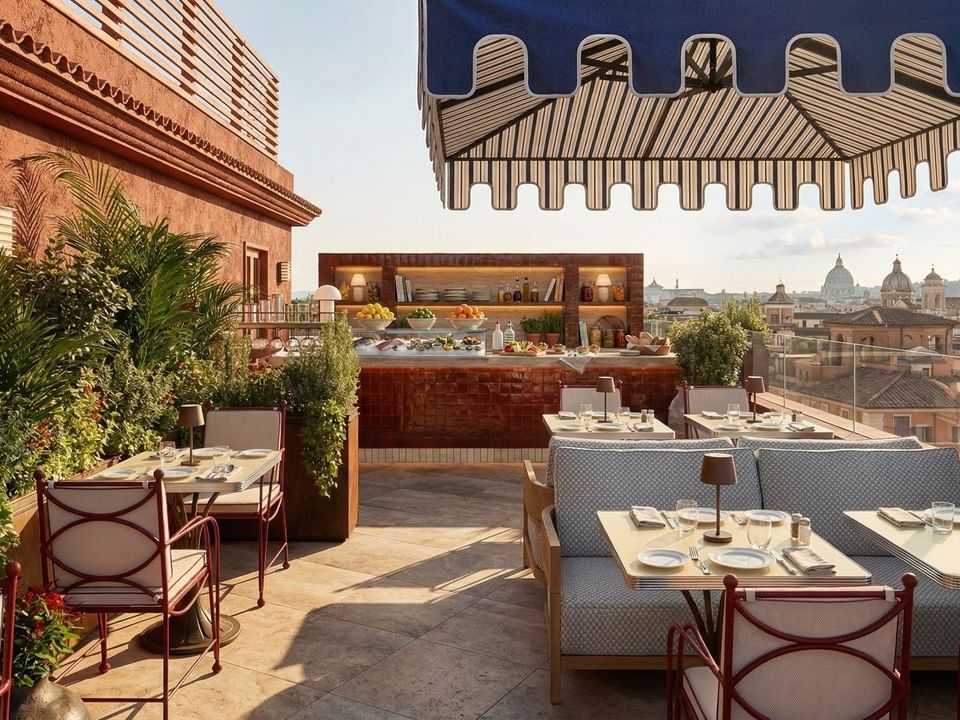 Outdoor dining tables beneath a striped awning in Lyve Rooftop Terrace at Thompson Rome, overlooking Rome view restaurants