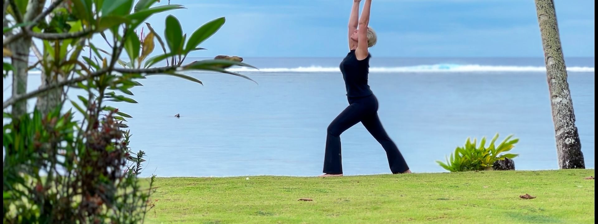 Guest practicing yoga by the calm sea under a cloudy sky on a green lawn at Warwick Hotels and Resort