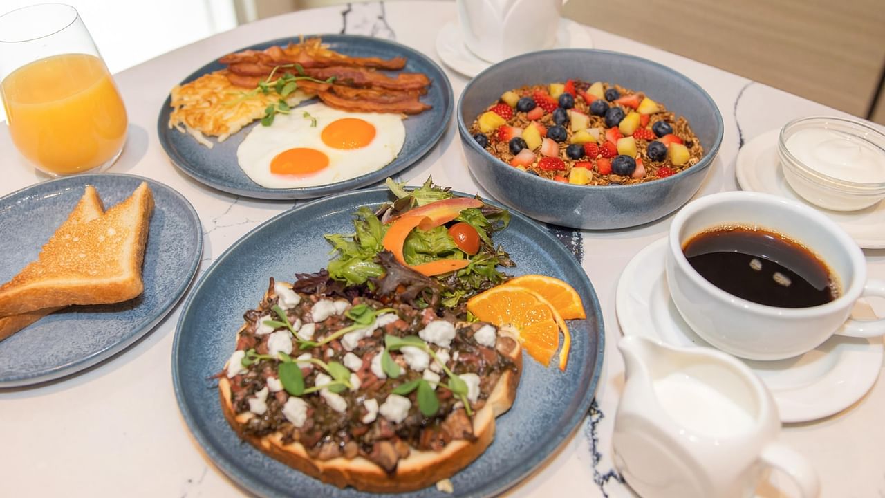 Breakfast spread with eggs, bacon, toast, fruit bowl, and drinks.