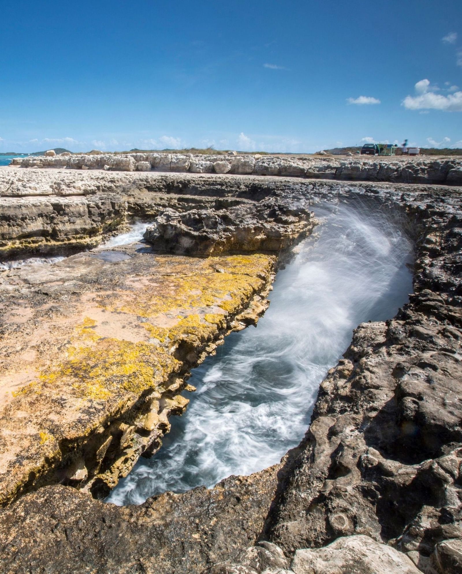 Turquoise water flows through a narrow rocky channel carved into limestone formations at Devil's Bridge under a clear blue sky.