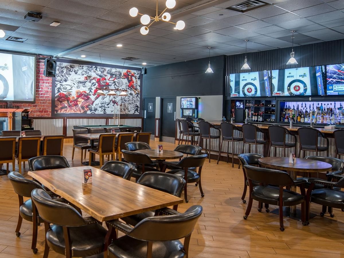 The Den Pub interior with tables, chairs, bar, and large screens playing sport channels.
