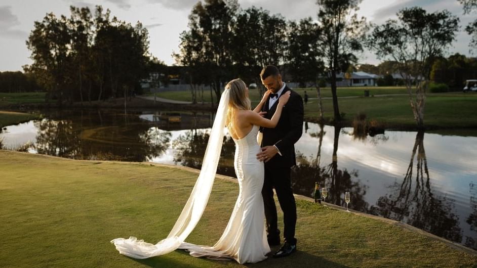 A bride and groom embrace by a lake at sunset, surrounded by trees near Mercure Kooindah Waters