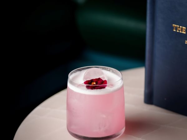 Pink cocktail with rose garnish and blue book titled THE at The Capital Hotel.