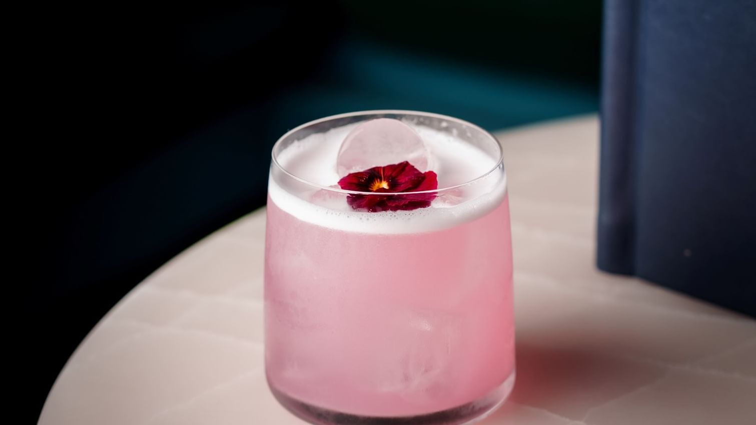A pink cocktail with a rose garnish next to a blue menu on a white table at Warwick Hotels and Resorts