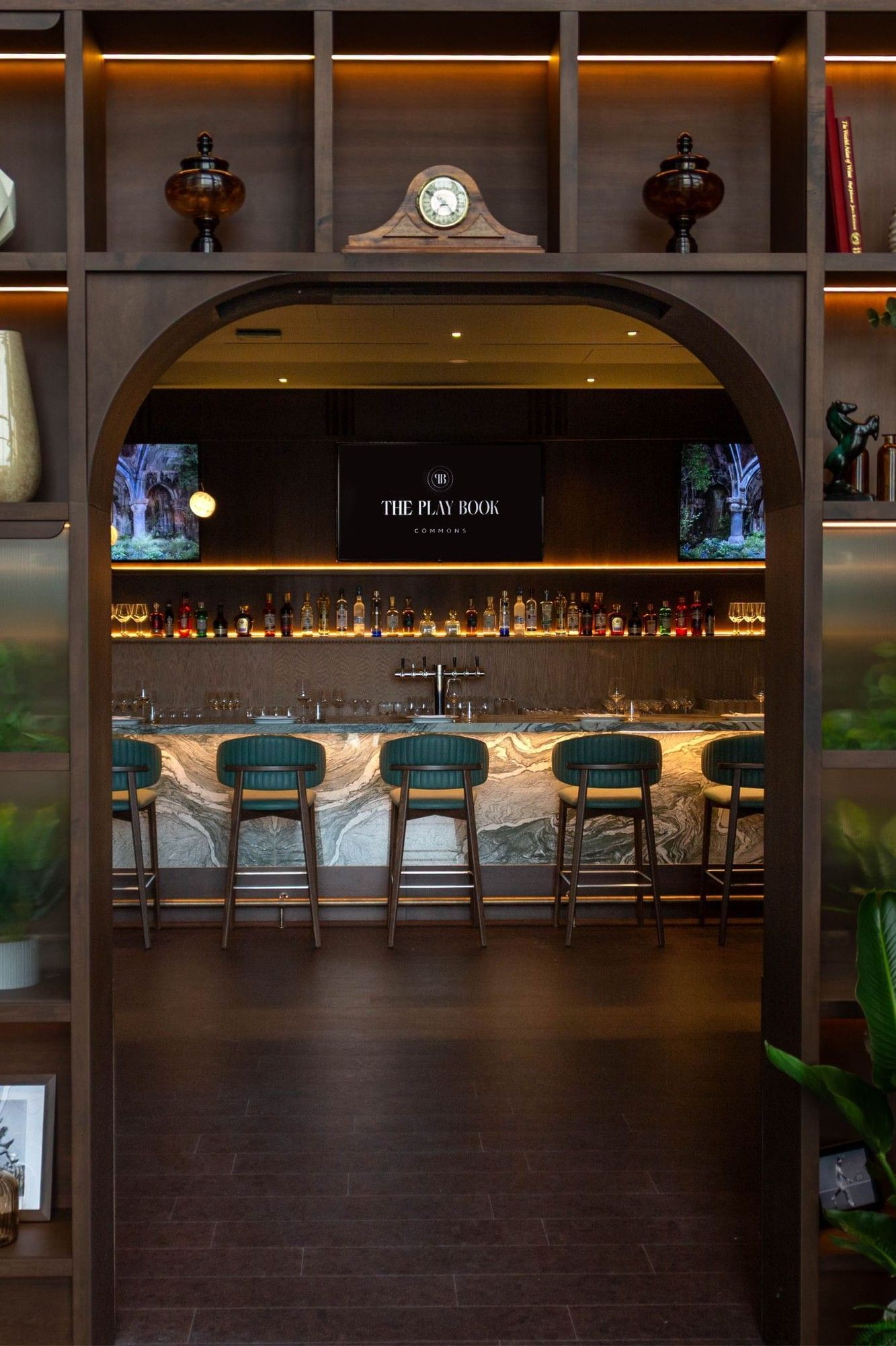 Hotel Bar at Hotel X Toronto, with green stools placed by a marble counter under an arched, plant-filled doorway