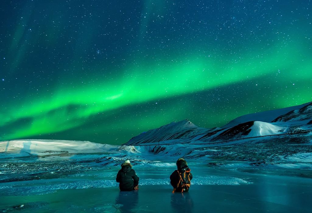 two people sitting looking at the Aurora Borealis or northern lights