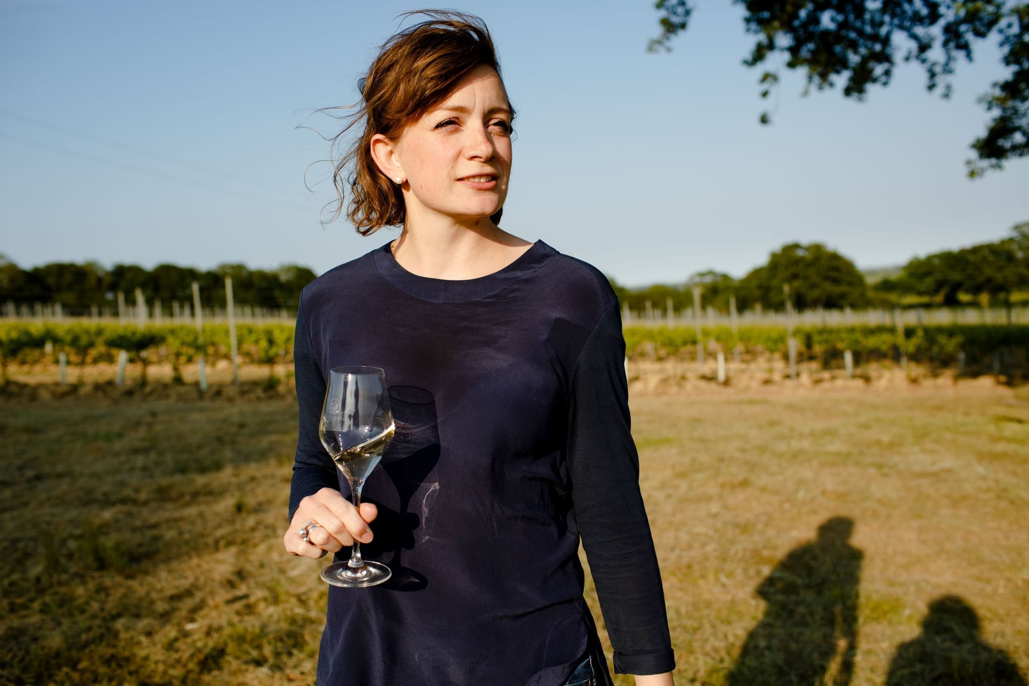 A lady holds a glass of wine in a serene field near The Londoner