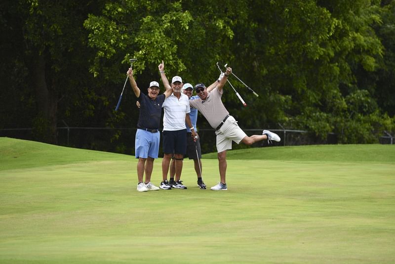 Four male golfers cheering and holding their clubs high on a vibrant fairway course at El Conquistador Resort