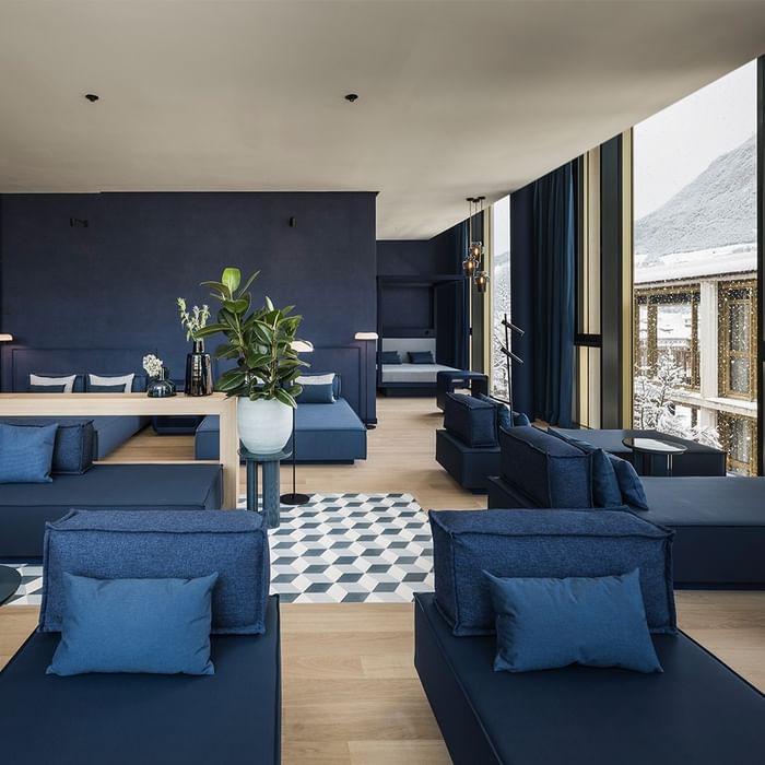 Blaues Wohnzimmer mit Sofas, Pflanzen, Teppich, Glaswänden und Ausblick auf verschneite Gebäude.