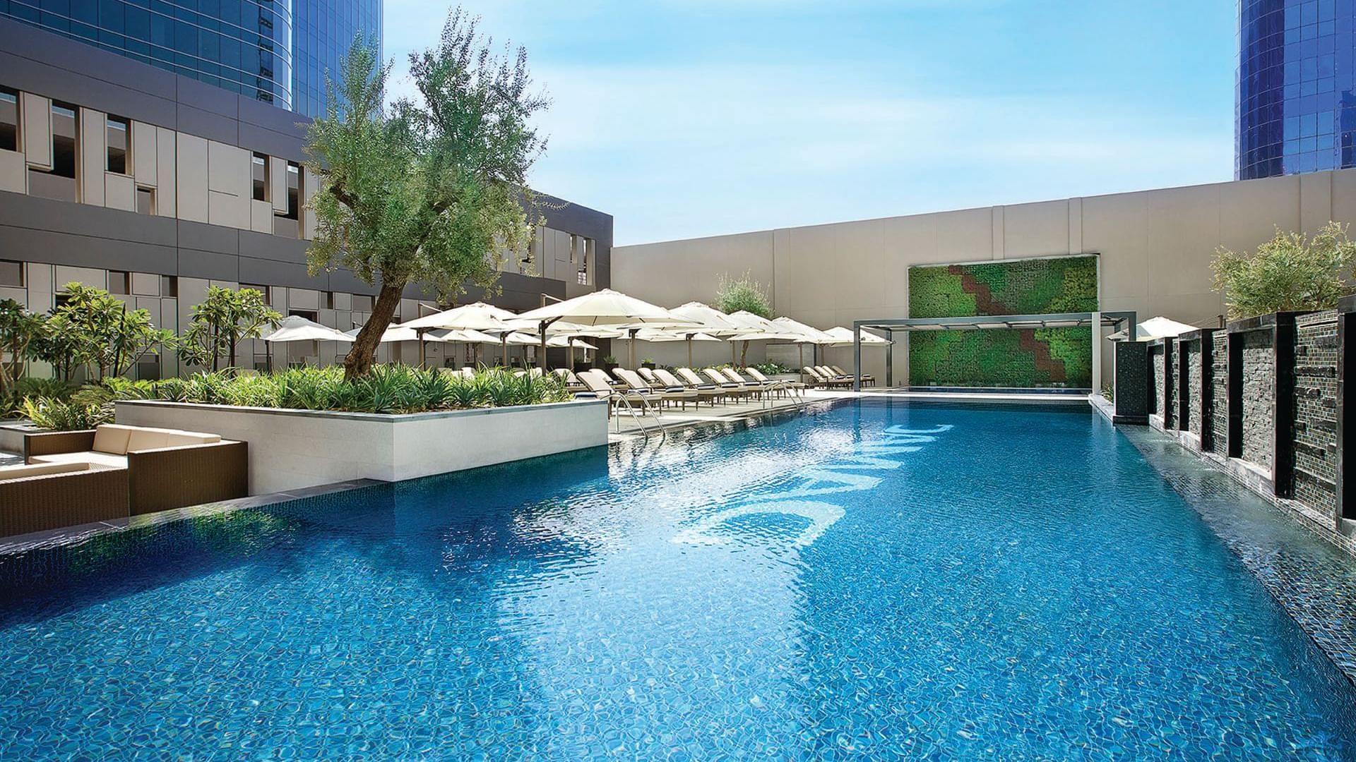 Outdoor pool area surrounded by cabanas & lounge chairs at DAMAC Maison Cour Jardin