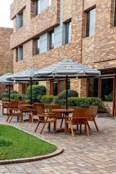 An outdoor patio at Habitel Hotel Select with wooden tables, chairs, and large striped umbrellas for shade
