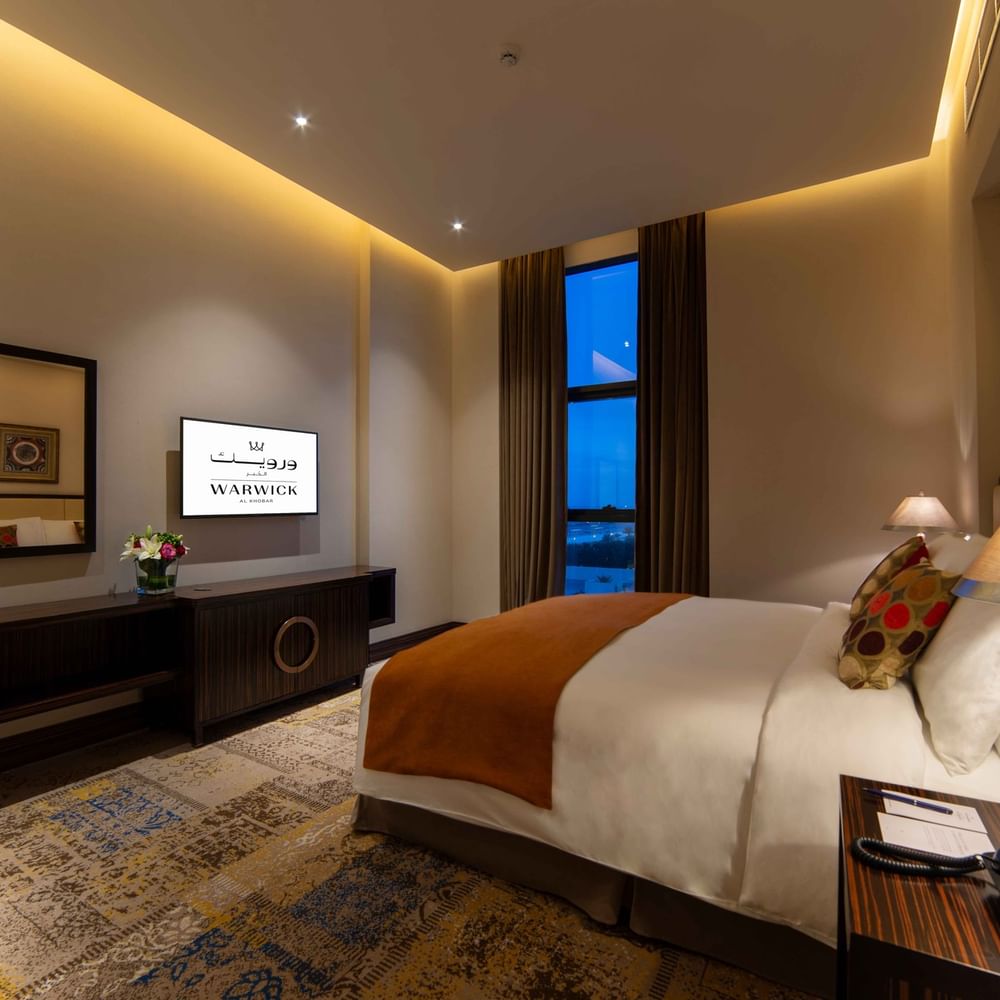 King bed by a dresser under a TV with a large mirror in Business Suite at Warwick Al Khobar