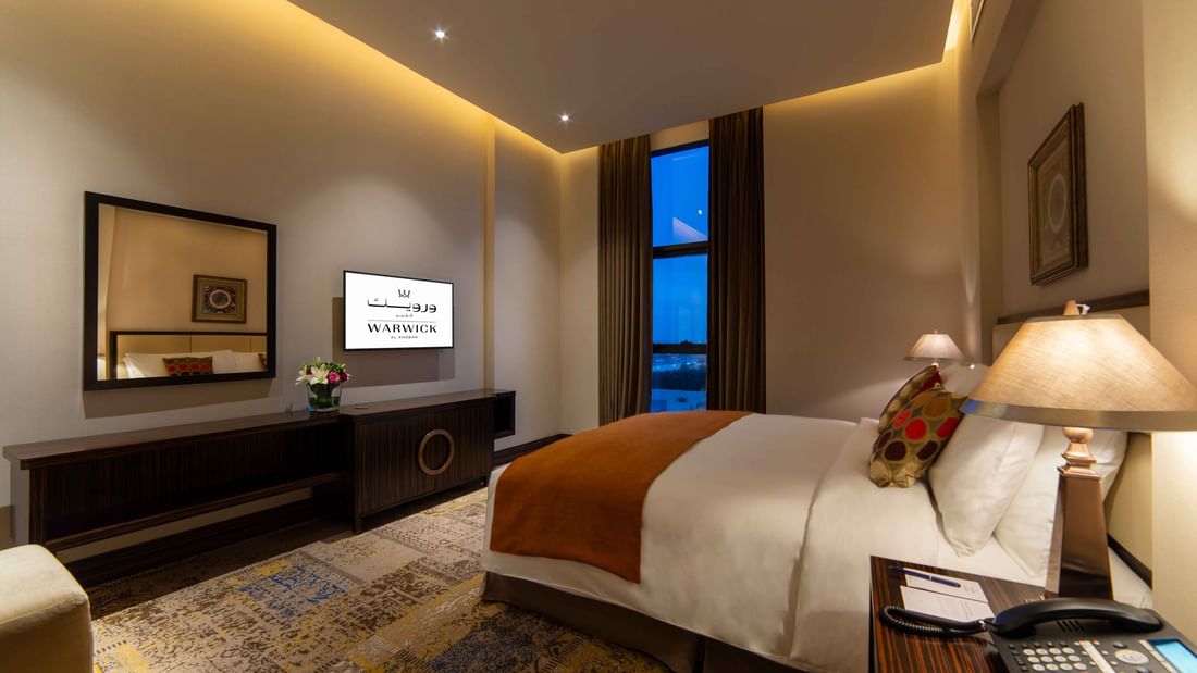 King bed by a dresser under a TV with a large mirror in Business Suite at Warwick Al Khobar