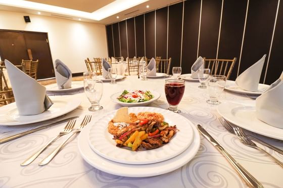 Mesa de comedor elegantemente puesta con manteles blancos, platos y comidas servidas en Araiza Calafia