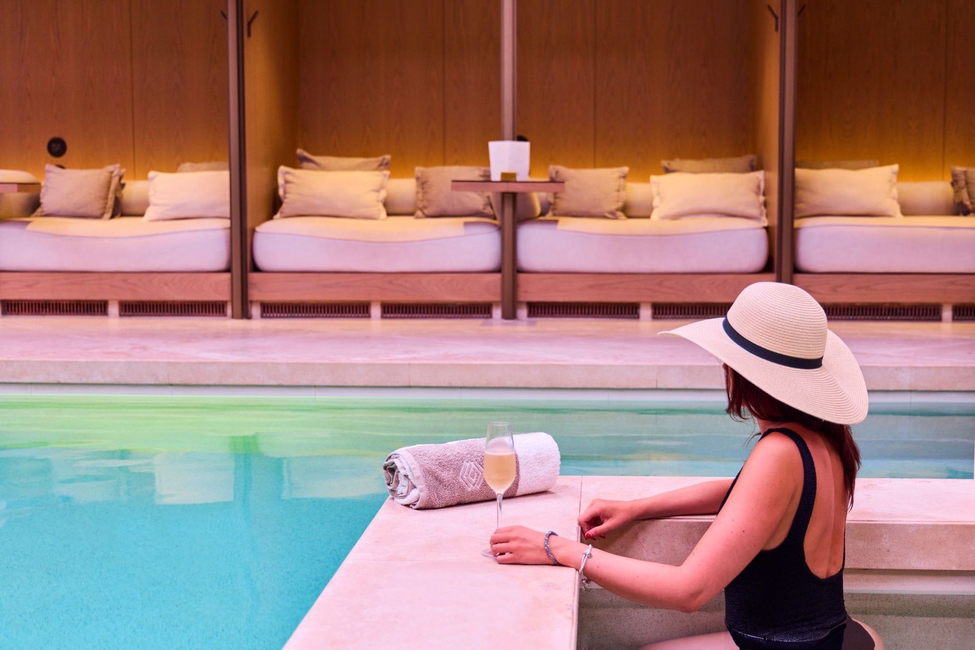 Une femme dégustant du champagne au bord d'une piscine, à côté de laquelle se trouvent des transats, à l'hôtel The Londoner