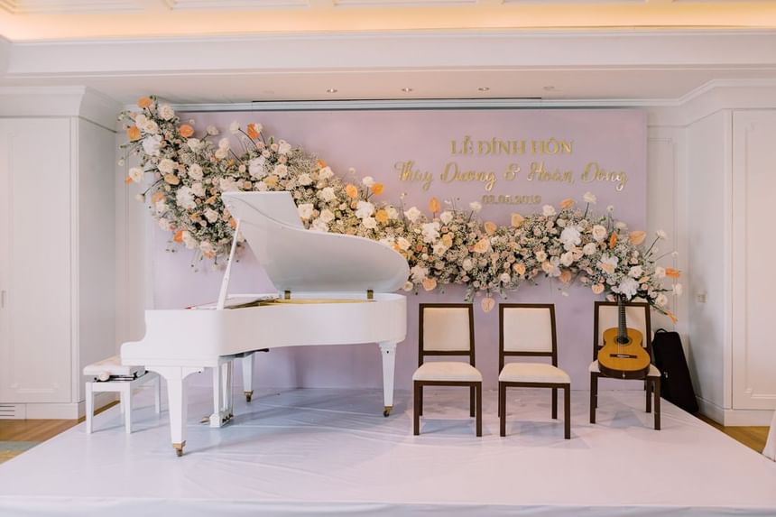 Elegant stage setup featuring a white grand piano, two empty chairs, guitar, and a floral backdrop at Park Hyatt Saigon