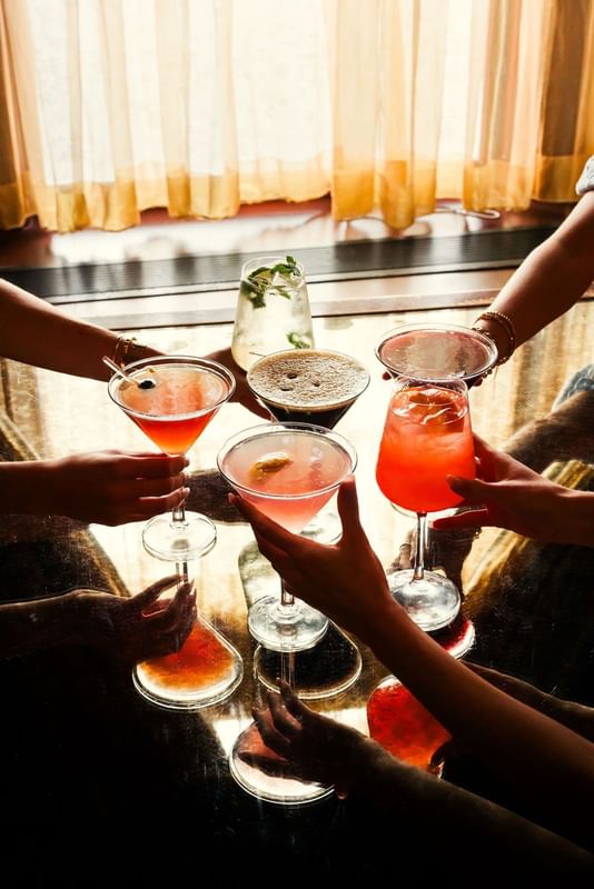 People holding colorful cocktails by a reflective table at Warwick Melrose Dallas