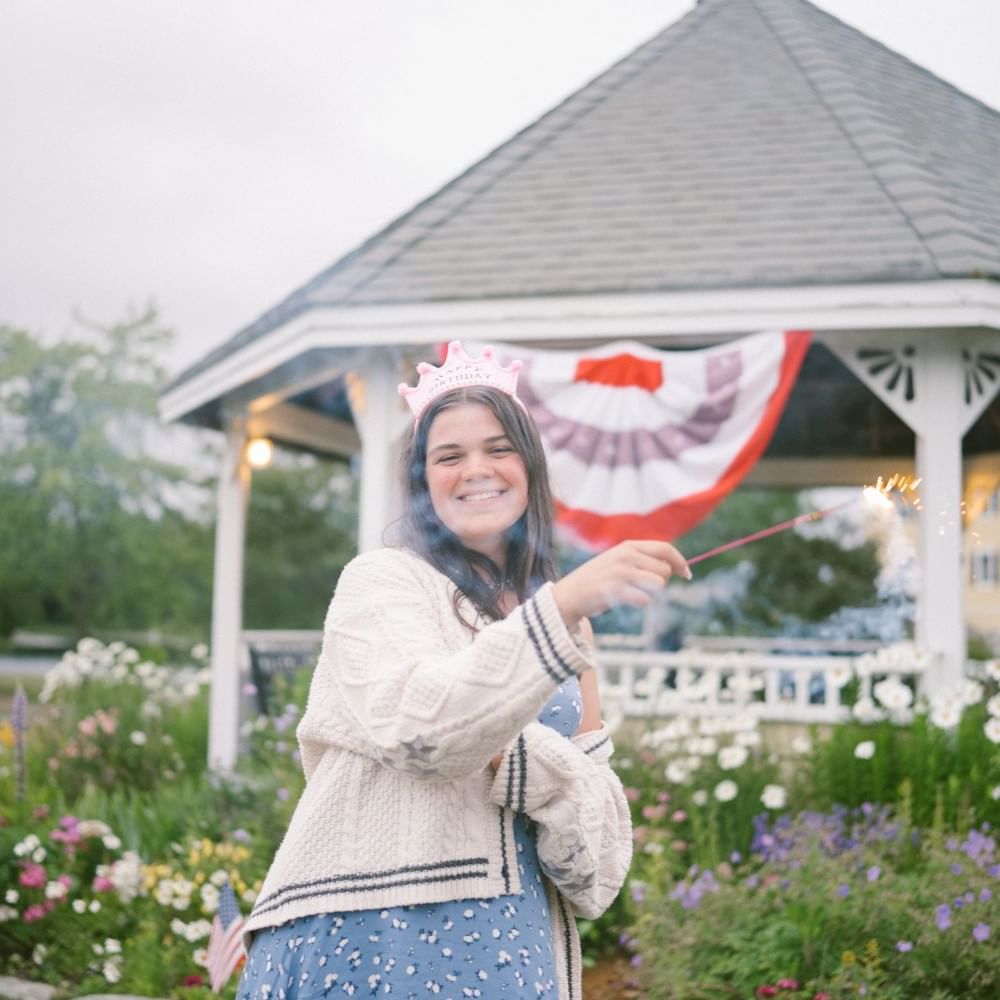 A lady in a blue dress waving a sparkler by the gazebo with flowers at The Bethel Inn Resort & Suites
