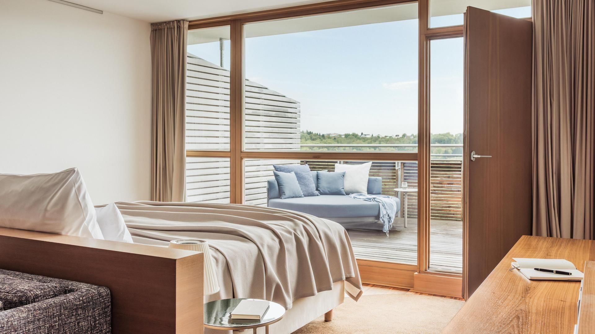 Modernes Schlafzimmer mit großem Bett, Balkon und Möbeln, durch große Fenster viel Licht.